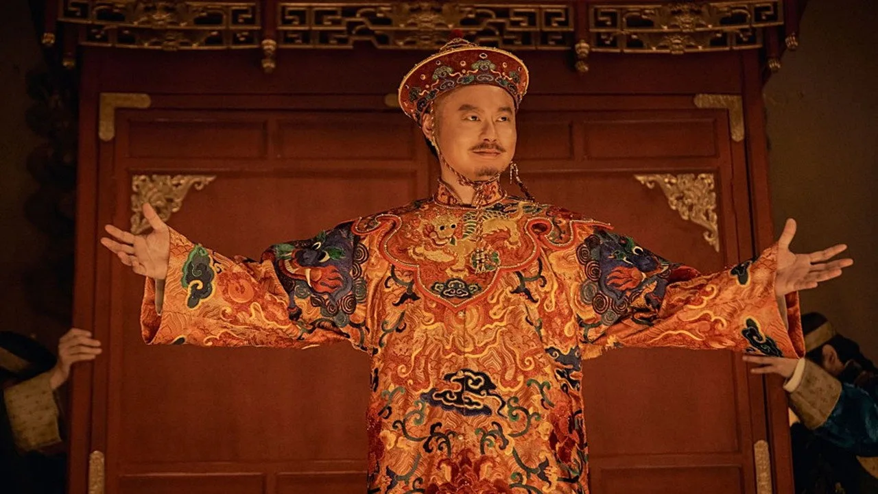 身穿红金色龙袍的男子在厅堂里张开双臂。